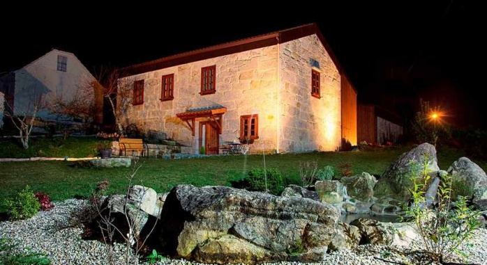 Con un estanque en primer plano, se ve el hotel rural A Cantaruxa Maruxa en medio de la foto en una escena nocturna preciosa. Siente Galicia.