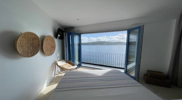 Habitación del hotel con encanto O Mar de Preciosa de la Costa da Morte. Se puede ver las vistas espectaculares al mar a los pies de la cama. Siente Galicia.